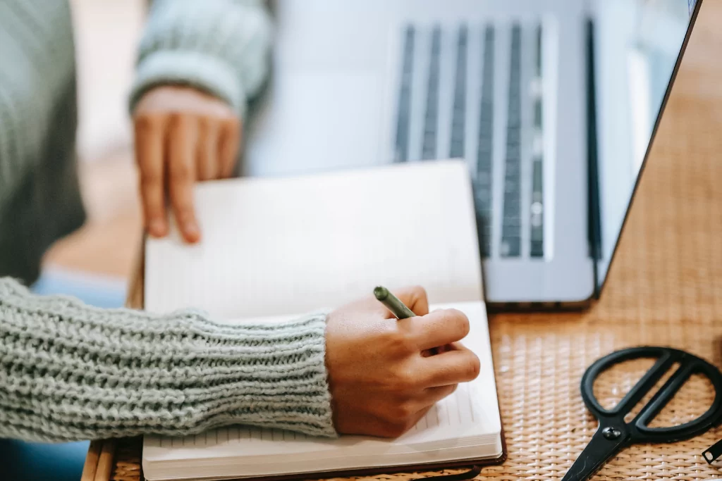 Mão de candidata fazendo anotações em seu caderno com caneta enquanto estuda análise sintática para concurso