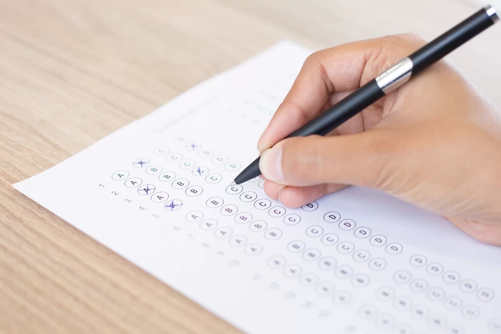 Mão de candidato de concurso público marcando no gabarito as respostas das questões de concordância verbal