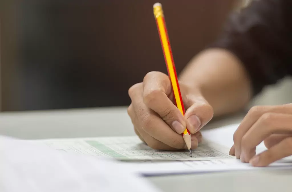 Mãos seguram um lápis grafite e marcam o gabarito de prova de uma das principais bancas de concurso público do Brasil