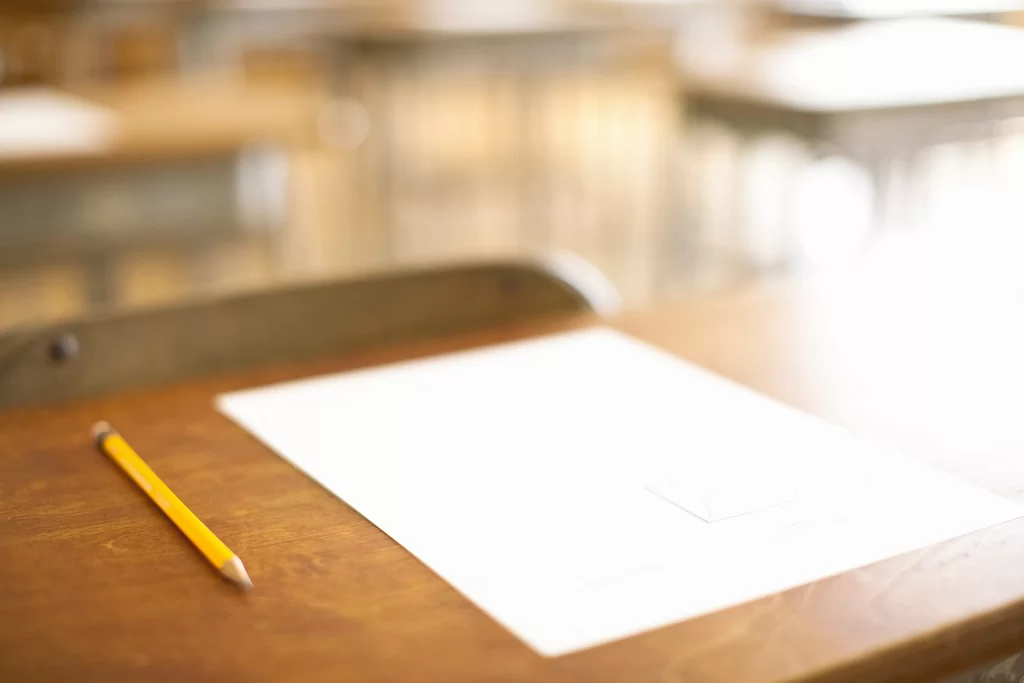 Folha de papel em branco ao lado de um lápis grafite amarelo em cima de uma mesa de madeira