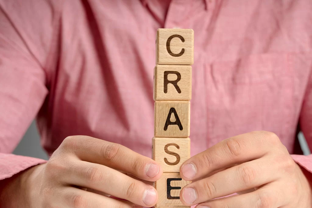 Mãos empilham pequenos blocos de madeira em que estão escritos letras que formam a palavra 'crase'