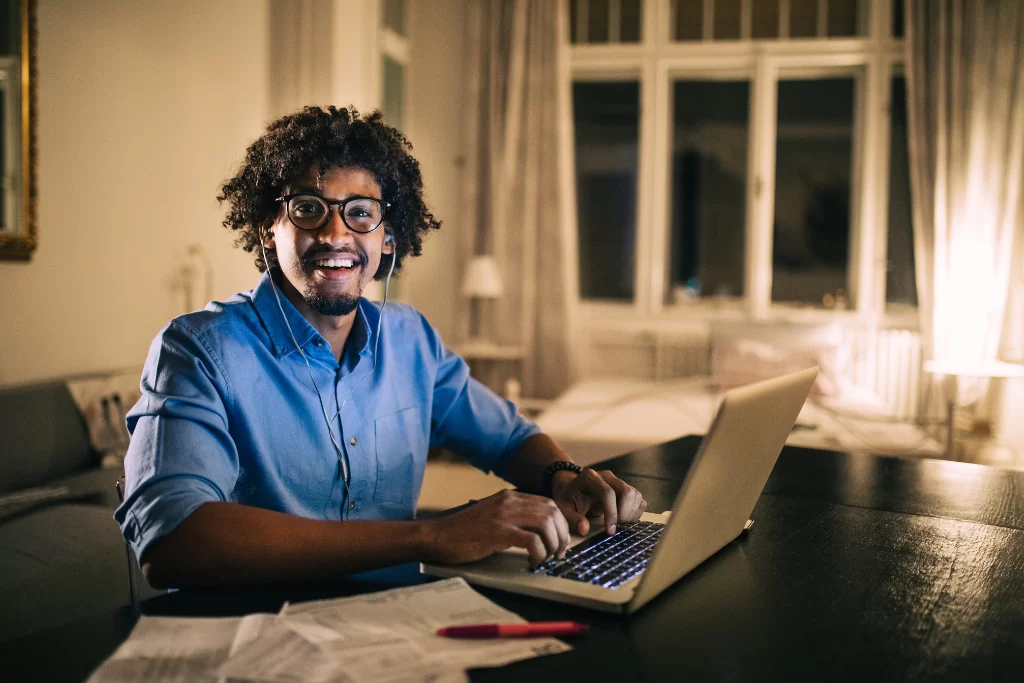 Concurseiro sorridente estuda usa notebook e papeis para estudar a diferença entre discurso direto e indireto