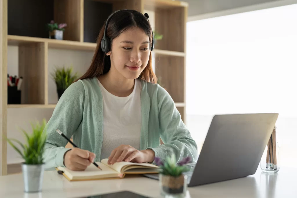Concurseira faz anotações no caderno e consulta um notebook enquanto estuda com modelos de questões da Vunesp