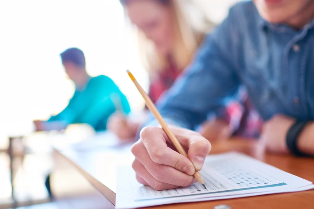 Mão segura um lápis grafite e marca no gabarito as respostas das questões de recorrência e inferência