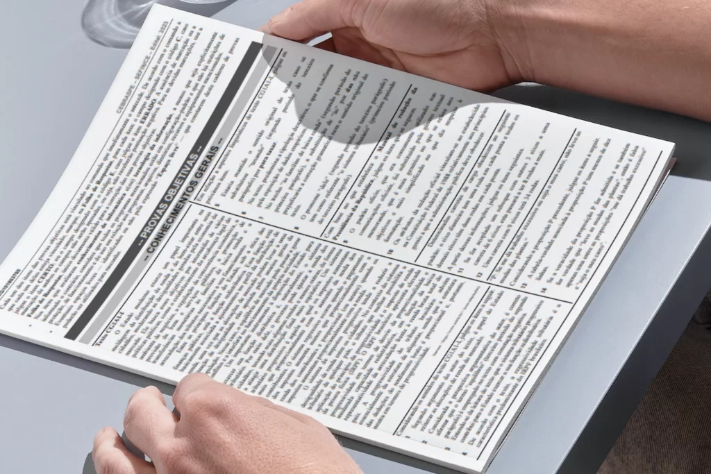 Mãos seguram prova com questões Cebraspe de concurso público por cima de mesa azul 