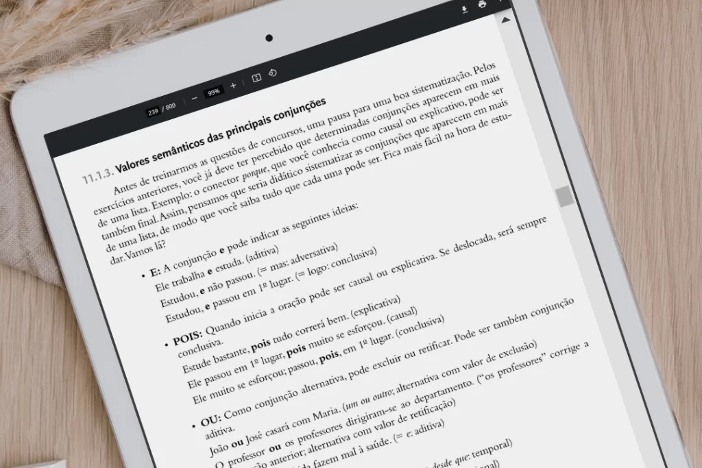 Página de livro virtual em e-reader branco sobre uma mesa de madeira onde se lê 'valor semântico das conjunções'