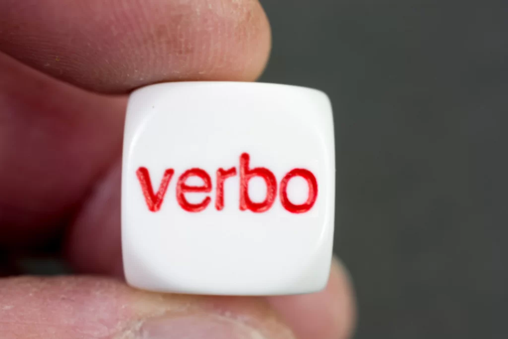 Mão segura dado branco com 'verbo' em vermelho sobre 'modo subjuntivo do verbo'