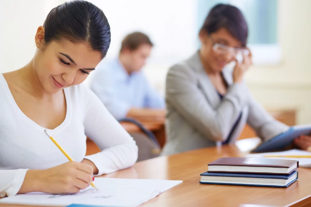 Concurseiras sorridentes resolvem exercícios sobre termos integrantes da oração em sala de aula.