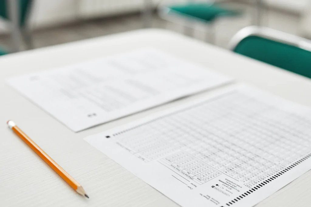 Gabarito de prova com questões de interpretação de textos para concurso, acompanhado por lápis amarelo e cadeiras verdes.