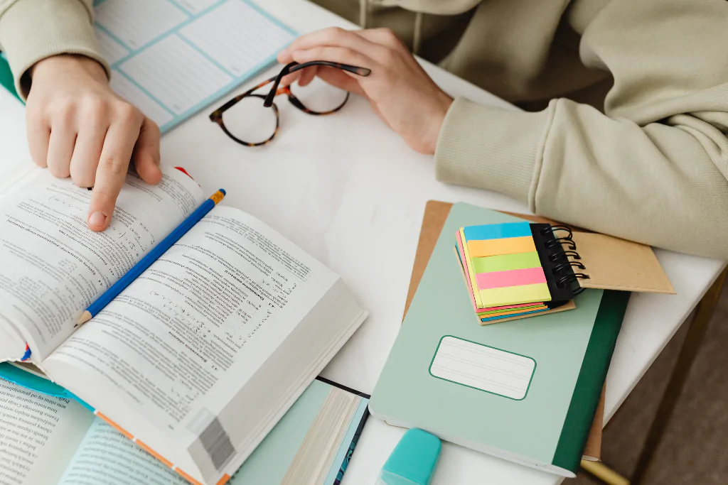 Concurseiro sentado em uma mesa de estudos, consultando um livro aberto de gramática enquanto estuda conjução integrante.