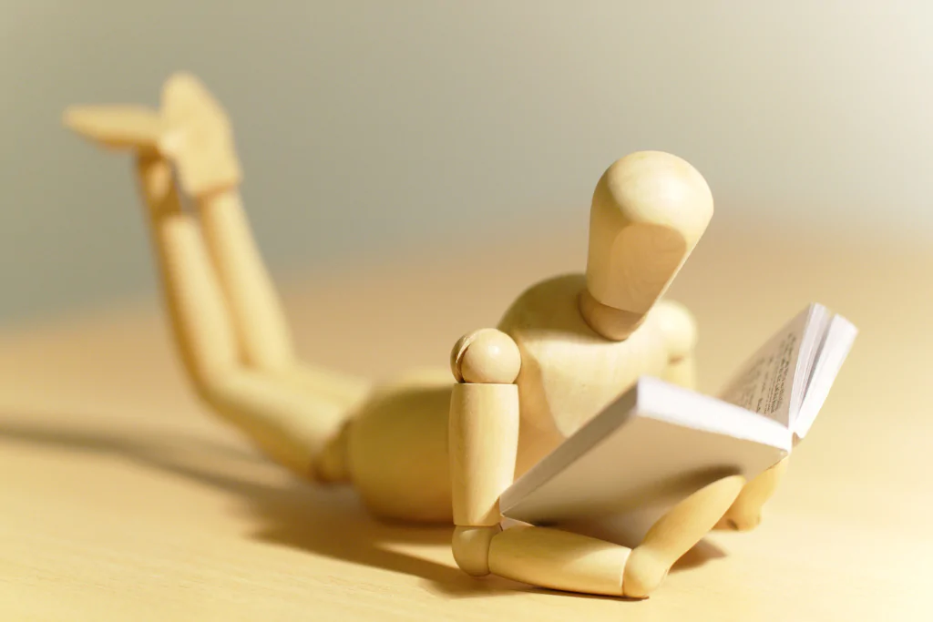 Boneco articulado de madeira lendo um livro em alusão ao concurseiro que estuda o que é coesão e coerência